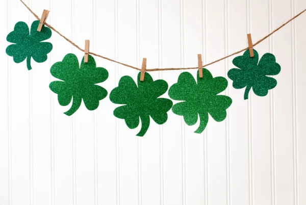 A string of green clothespins with four leaf clover decorations hanging from it.