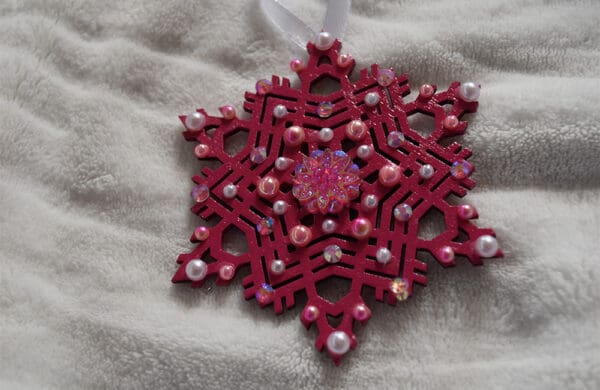 A red snowflake ornament with white beads on top of a blanket.