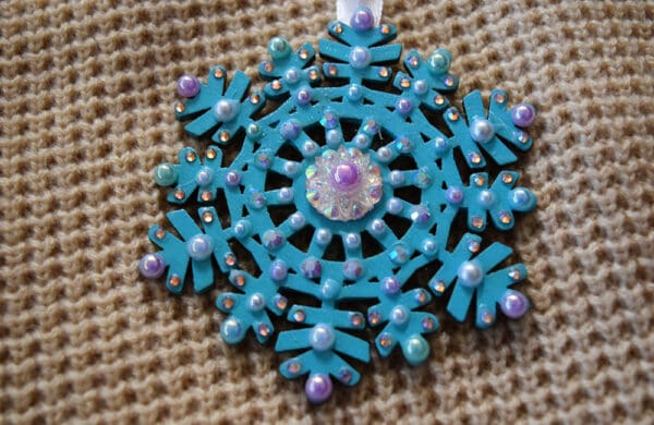 A blue snowflake ornament with purple and white beads.