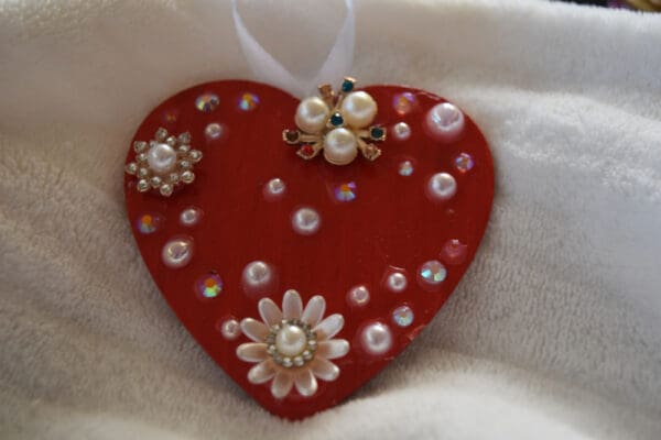 A red heart with white pearls and flowers on it.