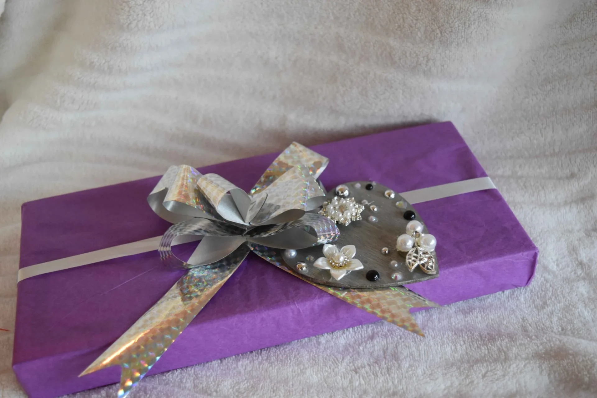 A purple gift box with silver ribbon and flowers.